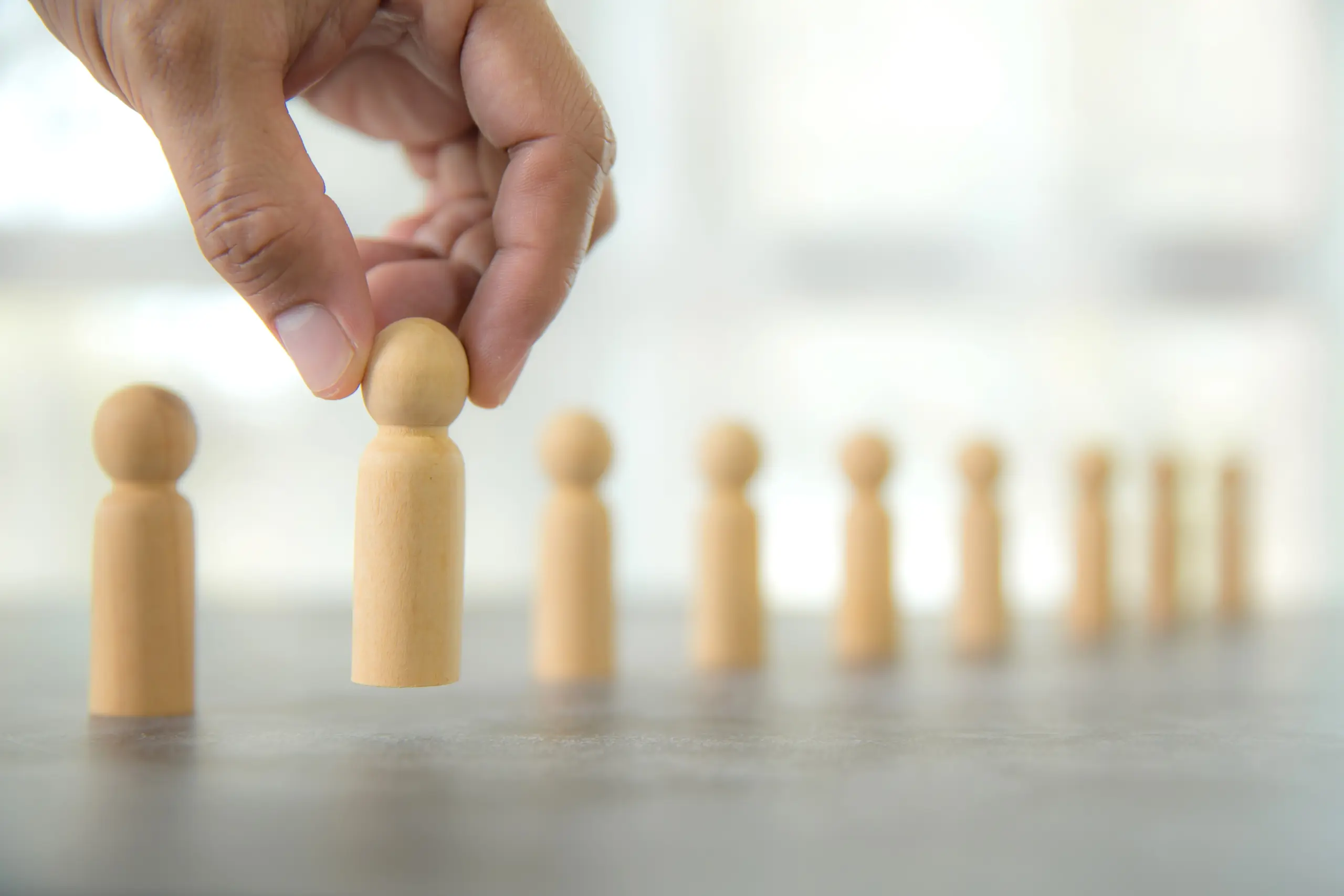 Table containing wooden pegs representing people with a hand picking up one of the pegs