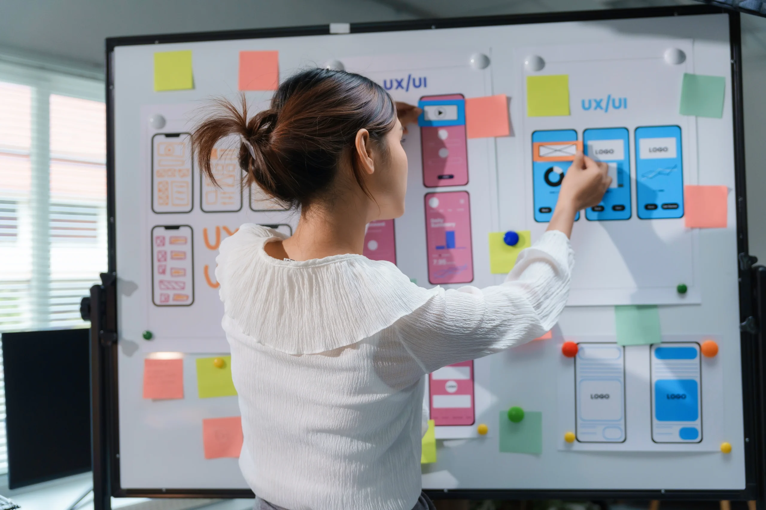 Young lady interacting with a whiteboard showing post-it notes and low fidelity smartphone diagrams