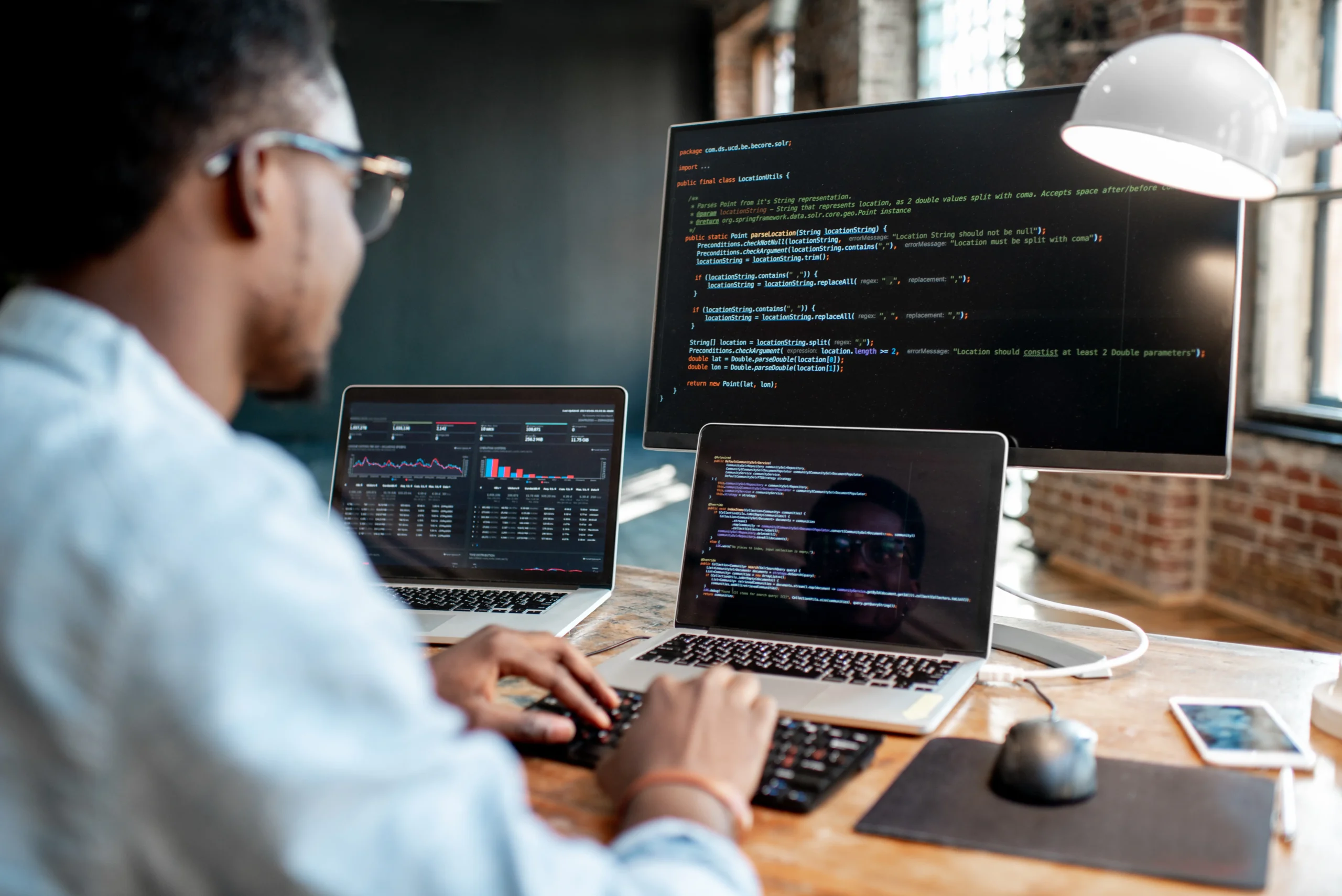 Man working a laptop with a large monitor placed behind it and another laptop to his left