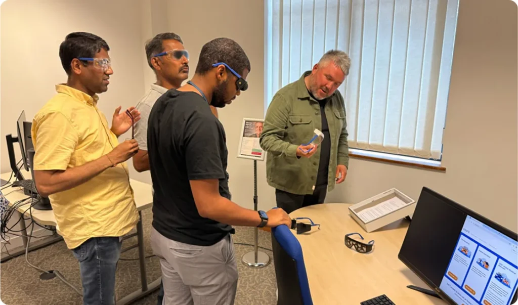 Four men in front of an empathy workstation trying on glasses to simulate different visual impairments