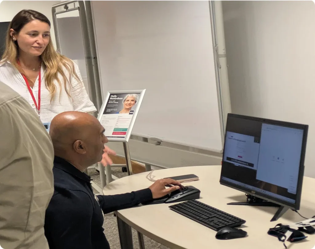 Seated man using a trackball at an empathy workstation, with a female demonstrator beside him