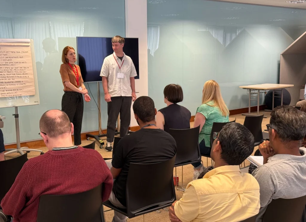 Crowd in a conference room watching a male and female presenter with a monitor and flipchart behind them