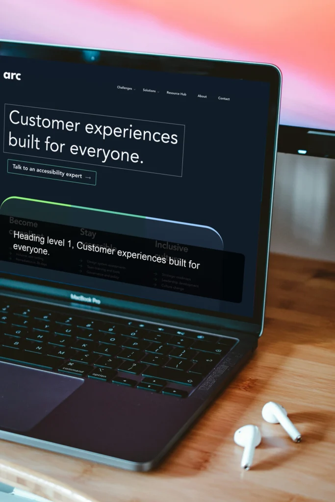 Laptop with screen showing website home page with headline "Customer experiences built for everyone", the user is using a screen reader, there are airpods to the side