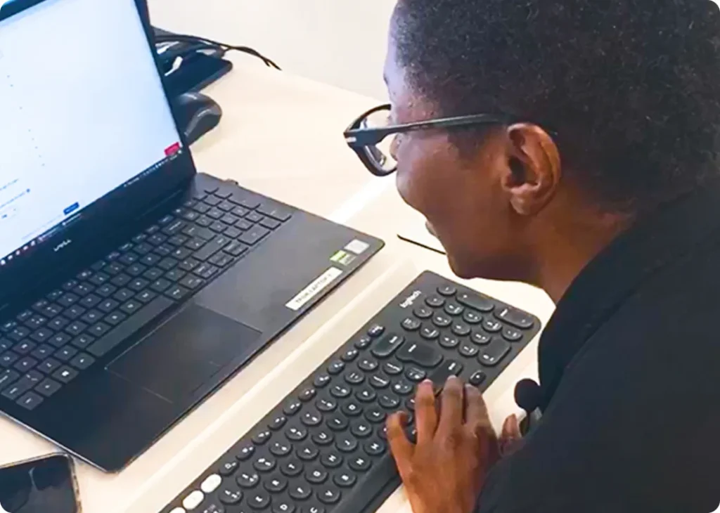 Woman seated at her desk, focused on her laptop screen with one hand on an external keyboard