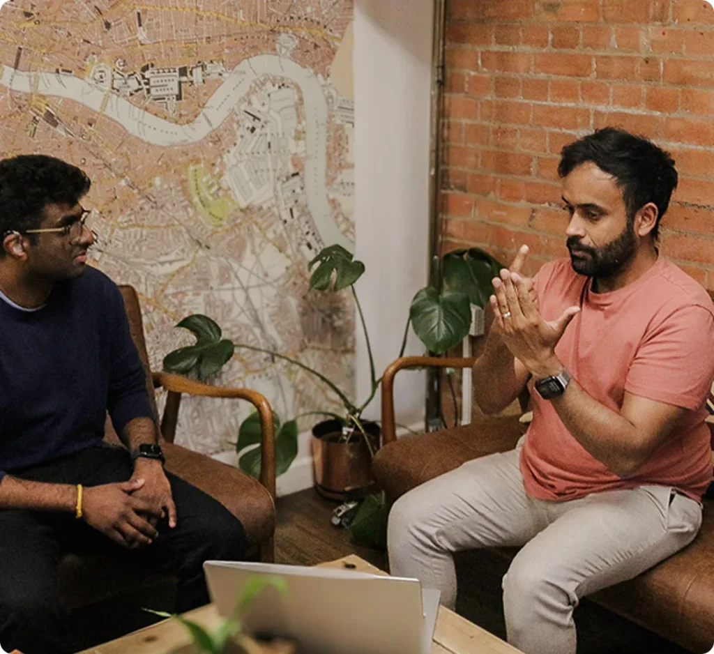 Two seated men using sign language across a coffee table with a laptop between them