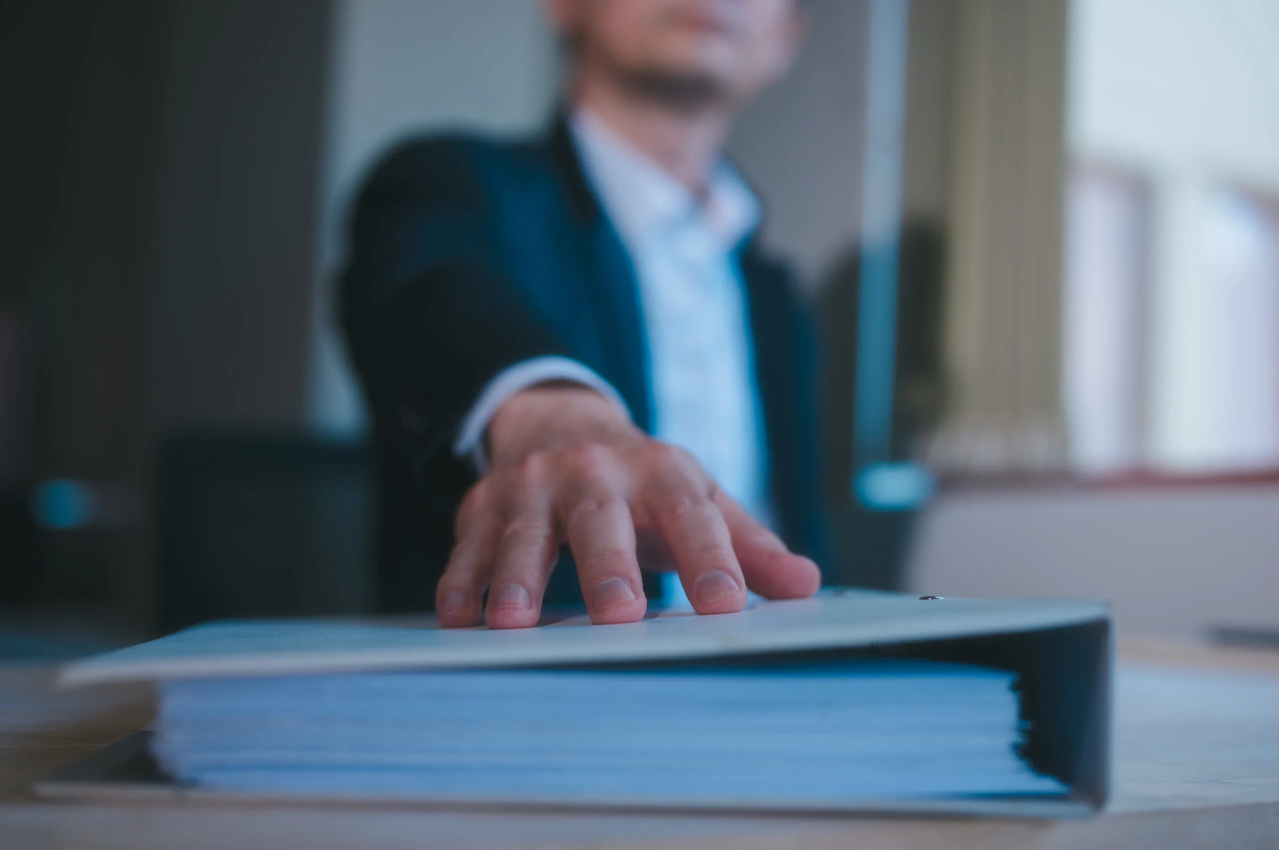 Close-up of a businessperson’s hand pressing down on a thick binder, symbolising a formal report or audit process.
