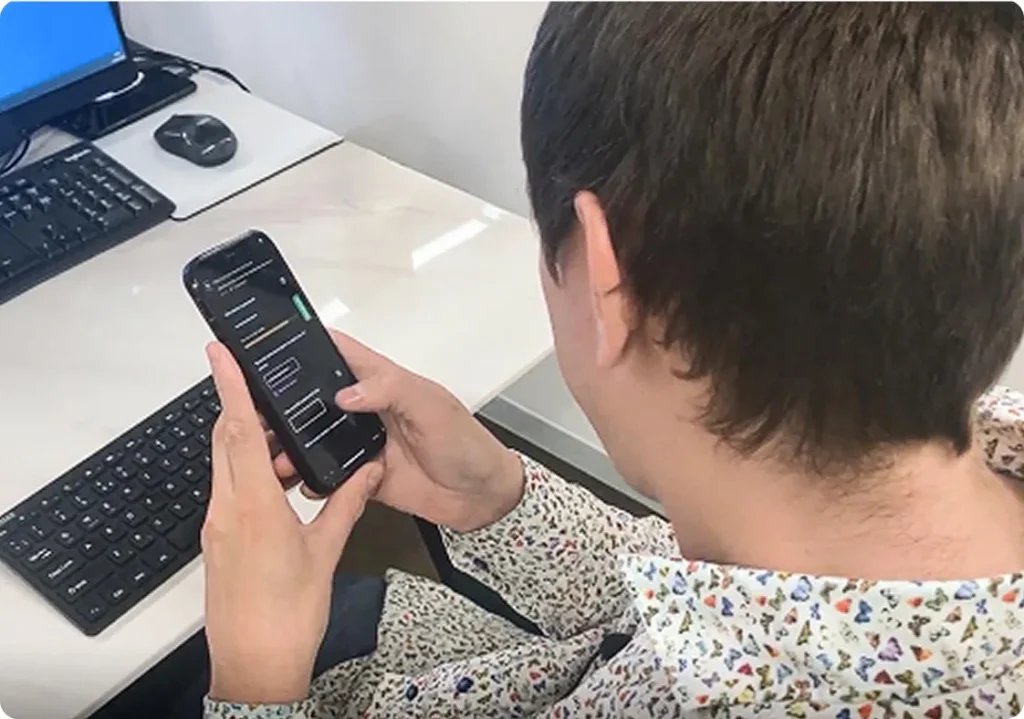 Man seated at a desk with a PC and two keyboards, interacting with a smartphone