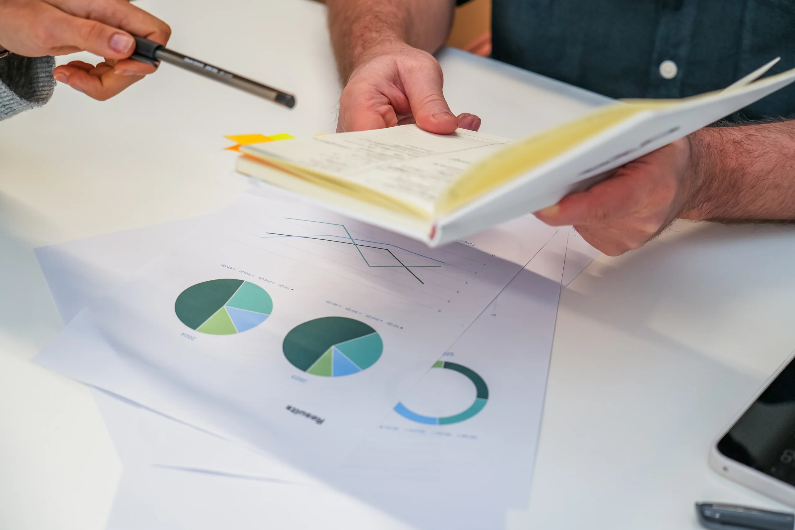 Close-up of hands reviewing a notebook and printed charts with pie and line graphs on a desk.