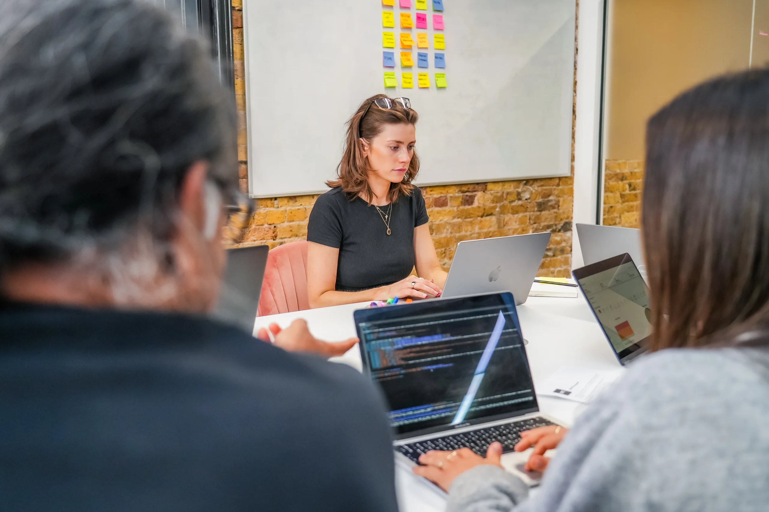 Team members collaborating with laptops during a coding session, with sticky notes on a whiteboard in the background.