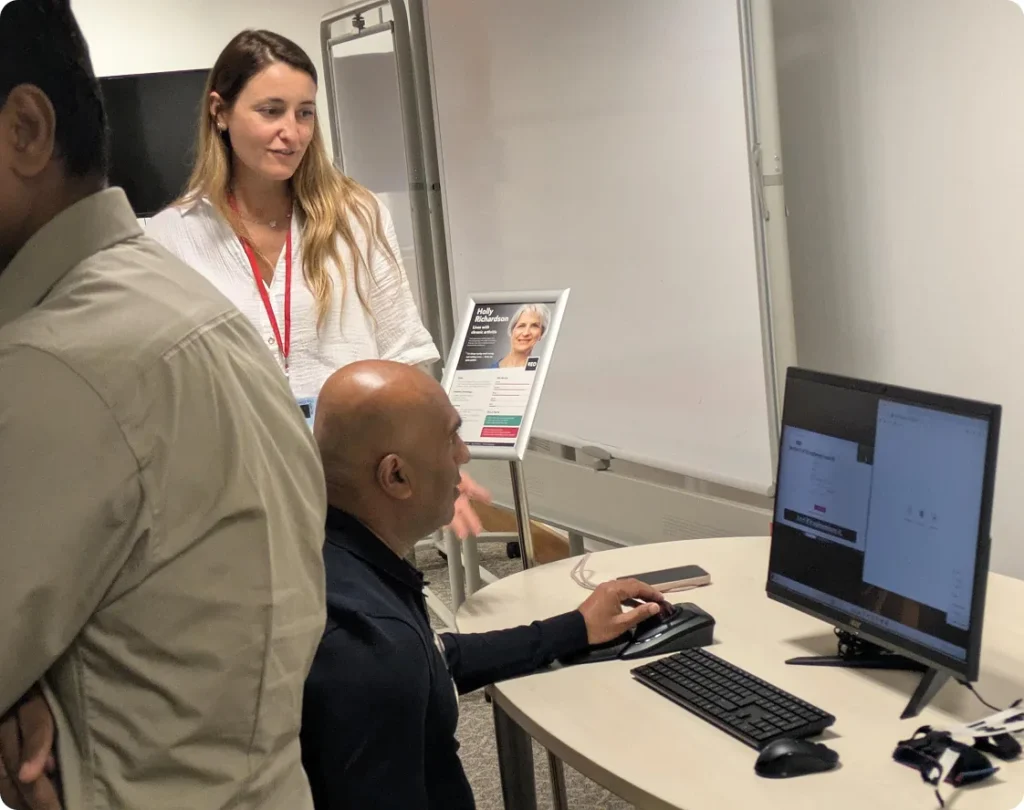 Seated man using a trackball at an empathy workstation, with a female demonstrator beside him