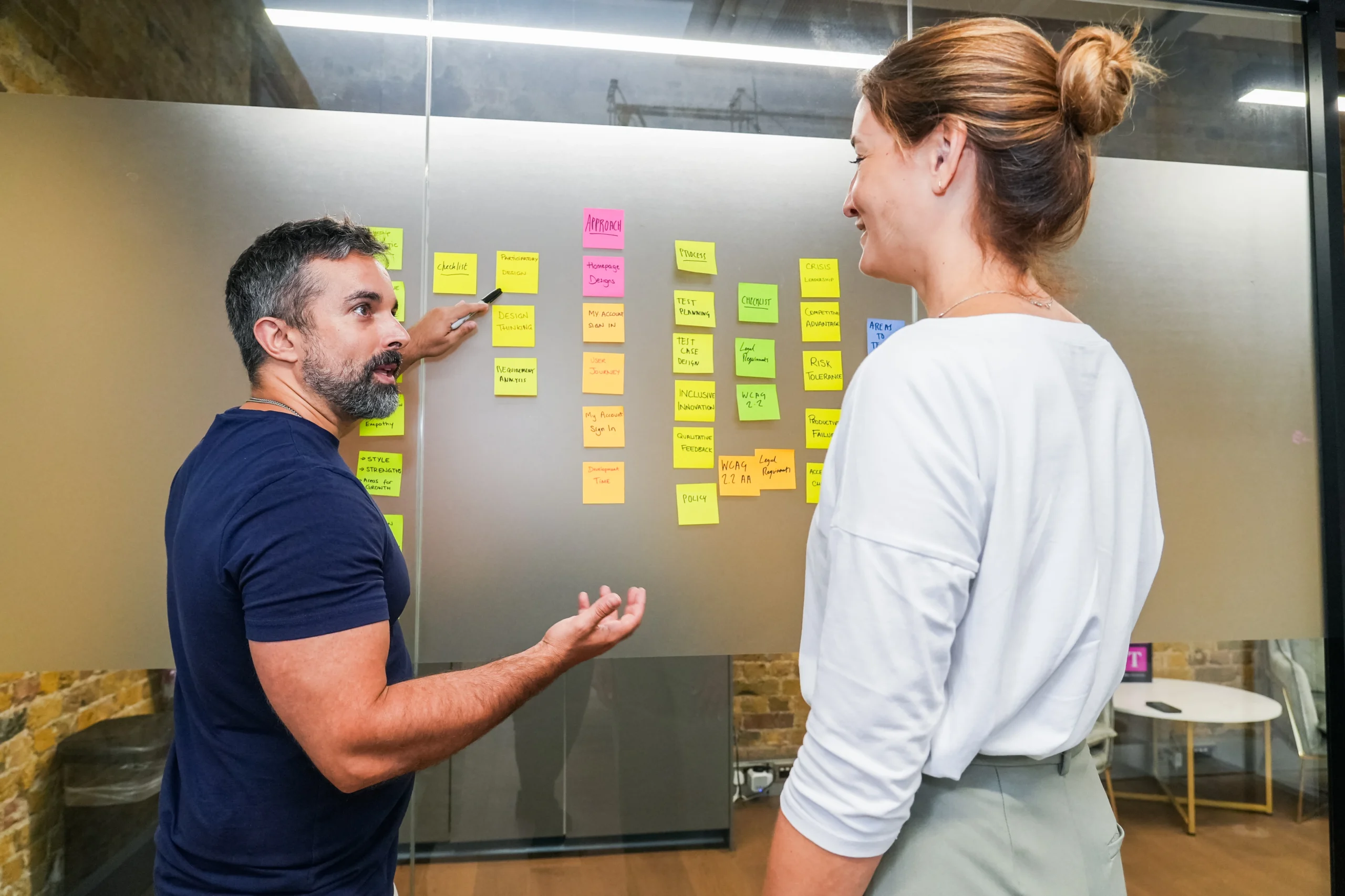 Two colleagues collaborate at a wall of sticky notes while mapping out an accessibility strategy.