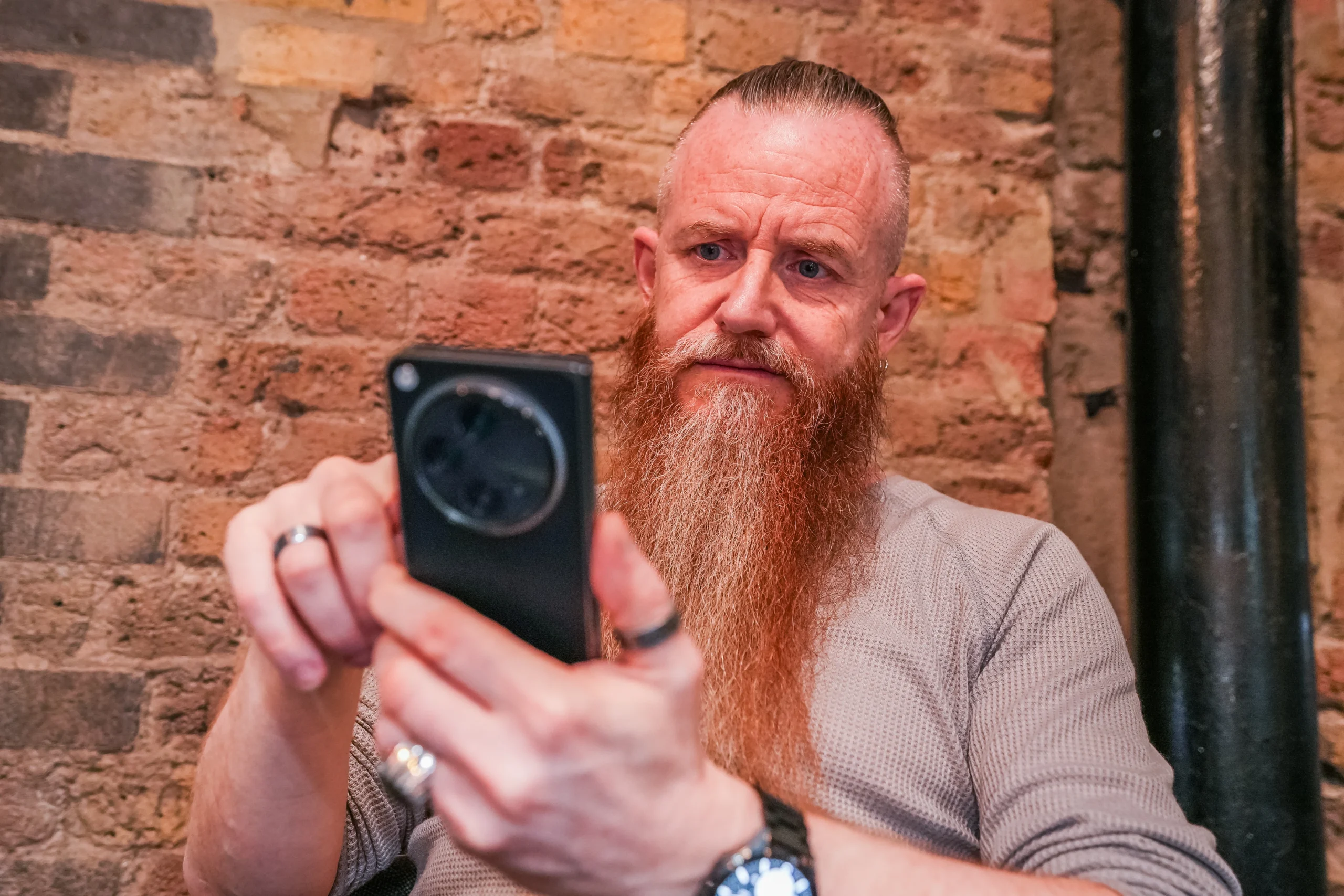A man with a long red beard closely examines his phone, testing accessibility features.