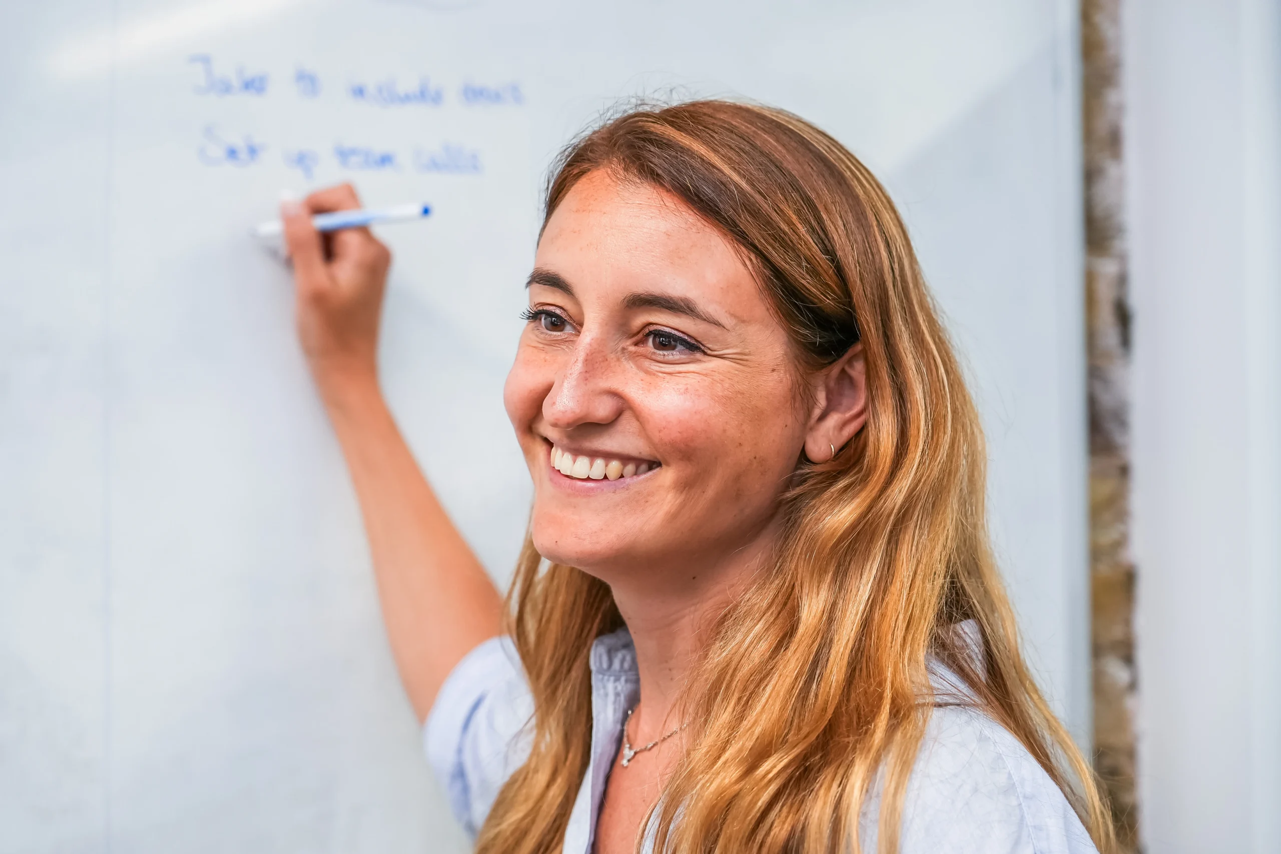 Smiling woman writes on a whiteboard during a content writing accessibility training session.