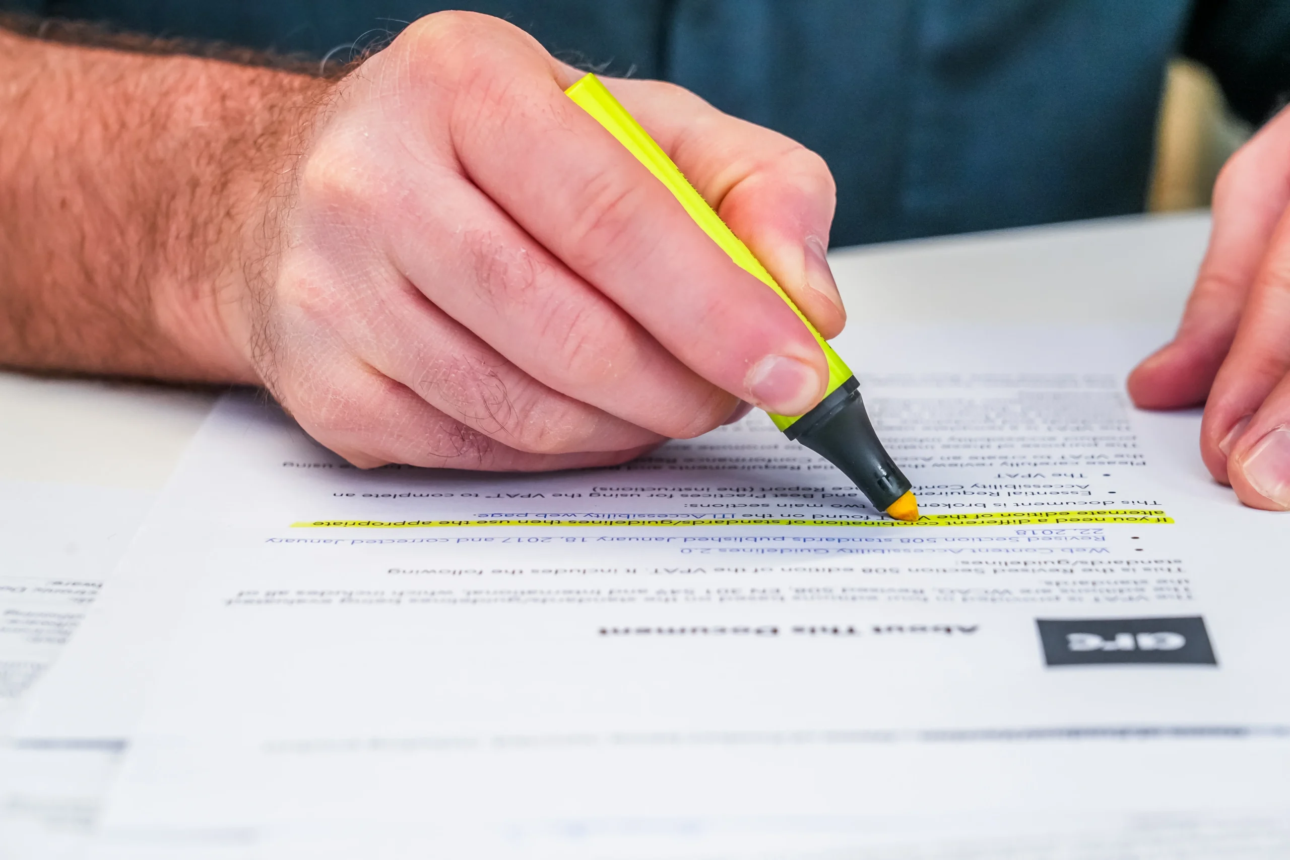 Close-up of a person using a yellow highlighter on an accessibility compliance document, highlighting key information.