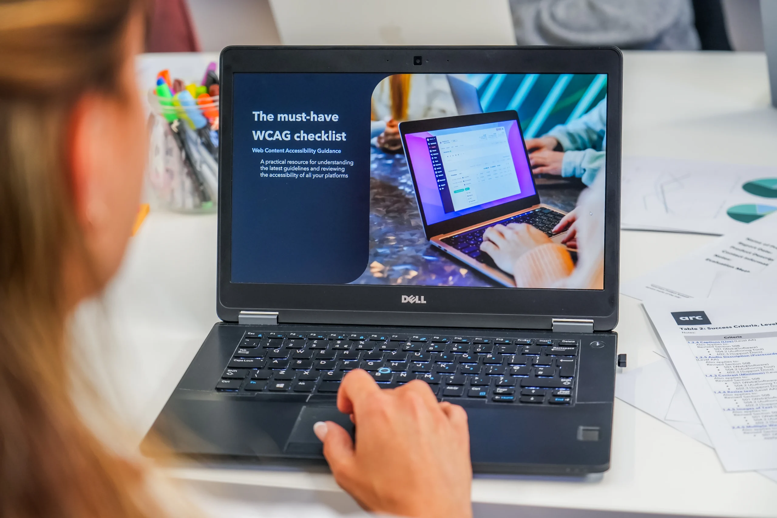 A person using a Dell laptop displaying a digital slide titled “The must-have WCAG checklist” with supporting text about accessibility guidelines.