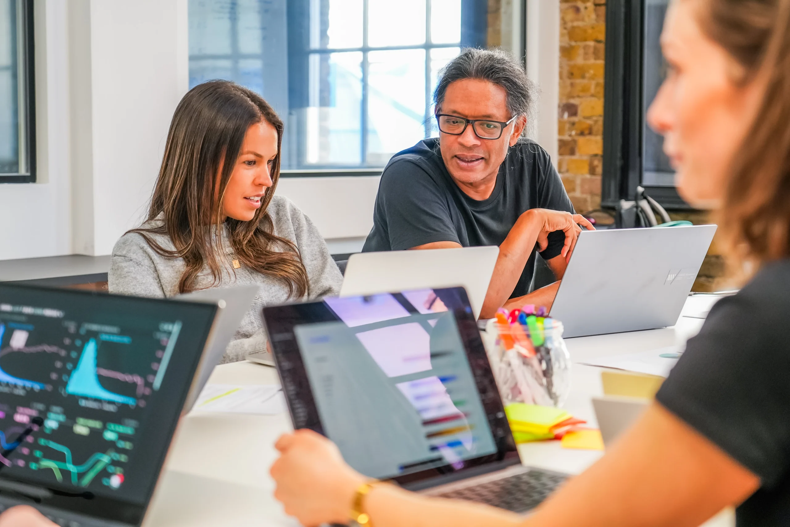 Two QA professionals sit at a desk with laptops, discussing data on-screen during a collaborative accessibility training session from an Arc Inclusion employee.